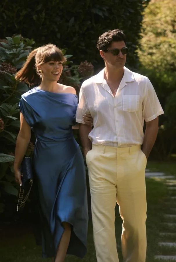 Casal de convidados em looks azul e bege, caminhando ao ar livre