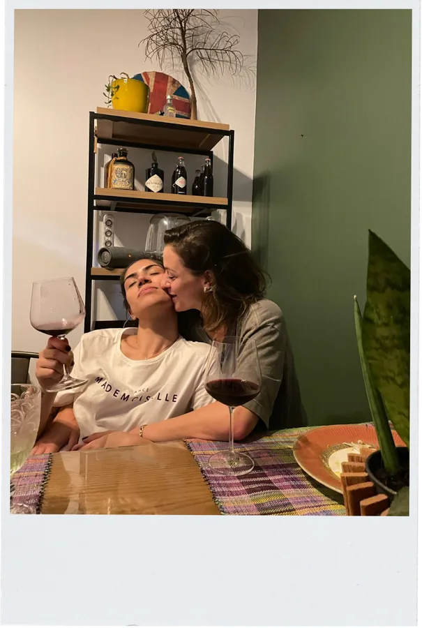 Bianca e Bruna brindando com taças de vinho à mesa