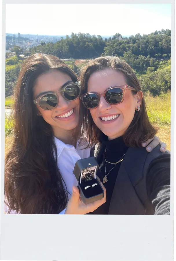Bianca e Bruna sorrindo ao ar livre mostrando o anel de noivado